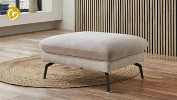 Moderner Hocker in hellem Stoffbezug mit schwarzen Metallfüßen – Teil einer Design-Sitzgruppe in einem stilvollen Wohnzimmer mit Holzlamellenwand, Holzboden und rundem Juteteppich, der Wärme und Natürlichkeit ausstrahlt.